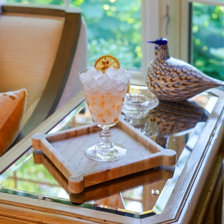 Cocktail with ice and a slice of lemon on a marble tray with a scenic background