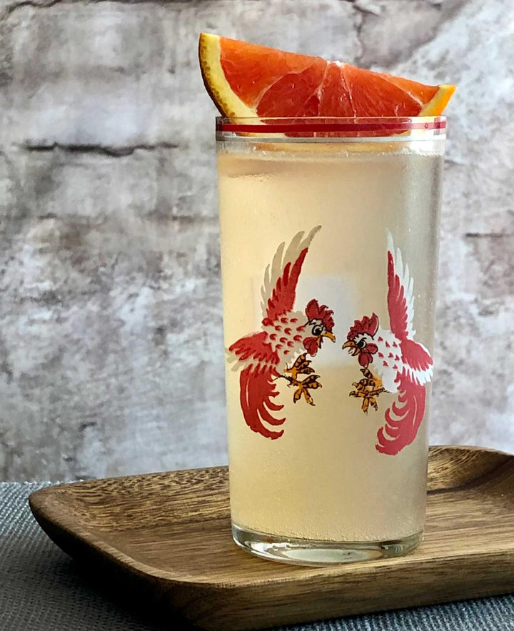 Cocktail in a glass with bird design on a wooden tray against a stone wall background