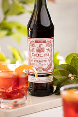 Bottle of Dolin Vermouth with a cocktail garnished with an orange peel on a blurred natural background