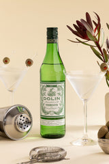 Green bottle of Dolin Vermouth with cocktail ingredients on a beige background