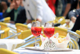 Two glasses of red cocktail on a table with blurred people in the background