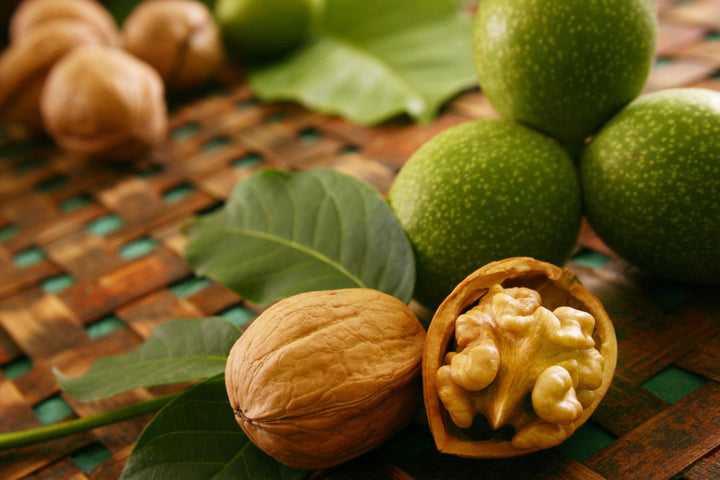 Walnuts with green shells and one open showing thekernel on a woven mat.