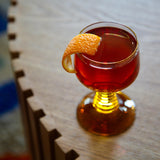 Glass of red liquid with an orange twist on a wooden surface
