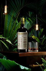 Hampden whisky bottle with a glass on a wooden surface surrounded by greenery