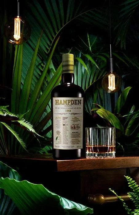 Hampden whisky bottle with a glass on a wooden surface surrounded by greenery