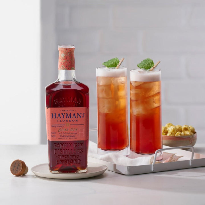 Bottle of Hayman's Aloe Gin with two glasses of iced tea on a white surface.