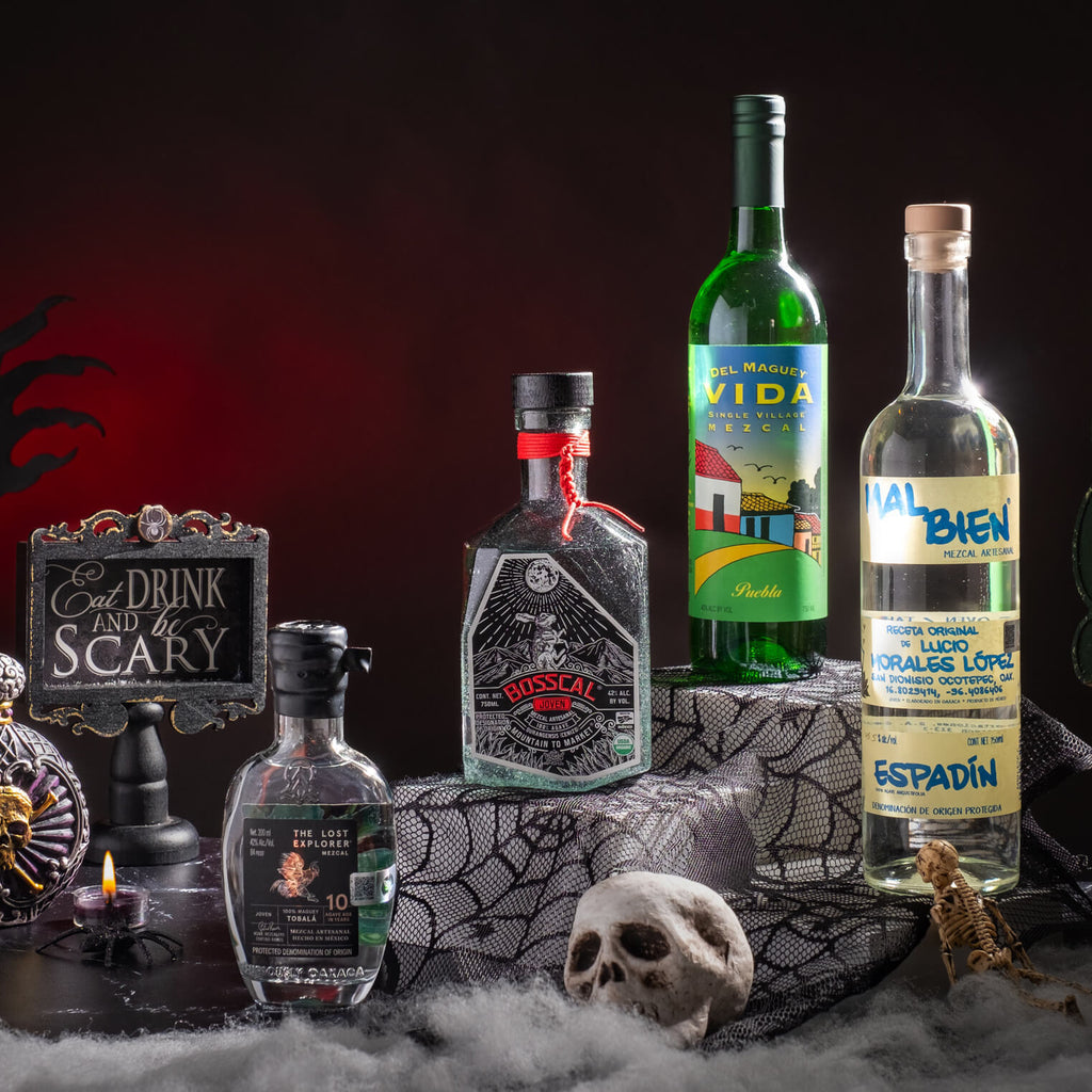 Bottles of The Lost Explorer Tobala Mezcal (200ml), Mal Bien Espadín Mezcal, Del Maguey VIDA Puebla Mezcal, and Mezcal Bosscal Joven on a Halloween themed tablescape.