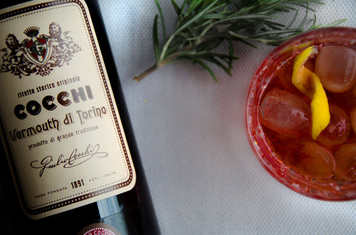 Cocchi Vermouth di Torino bottle with a glass of red liquid and garnish on a white surface