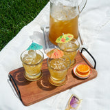 Four glasses of iced tea with lemon slices on a wooden tray outdoors.