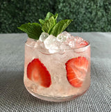 Cocktail with strawberries and mint leaves in a glass on a textured surface.