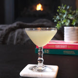 Cocktail in a glass on a marble coaster with a fireplace and books in the background