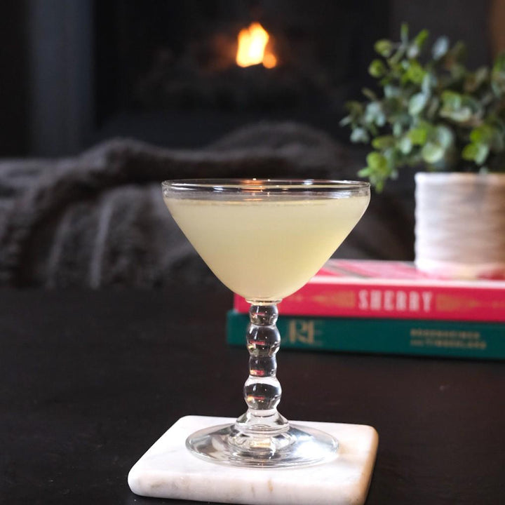 Cocktail in a glass on a marble coaster with a fireplace and books in the background