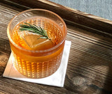 Orange cocktail with a lemon slice and rosemary garnish on a wooden surface