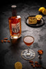 Bottle of Sagamore Spirit Rye Whiskey on a dark table next to a cocktail, fruit and bread.