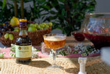 Liber & Co. Caramelized Fig Syrup bottle with a glass of amber-colored drink on a table outdoors.