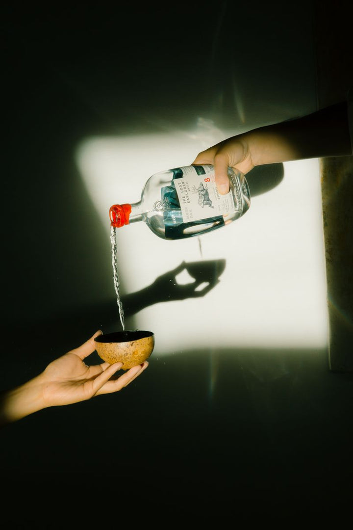 Person pouring liquid from a bottle into a small cup against a dark background