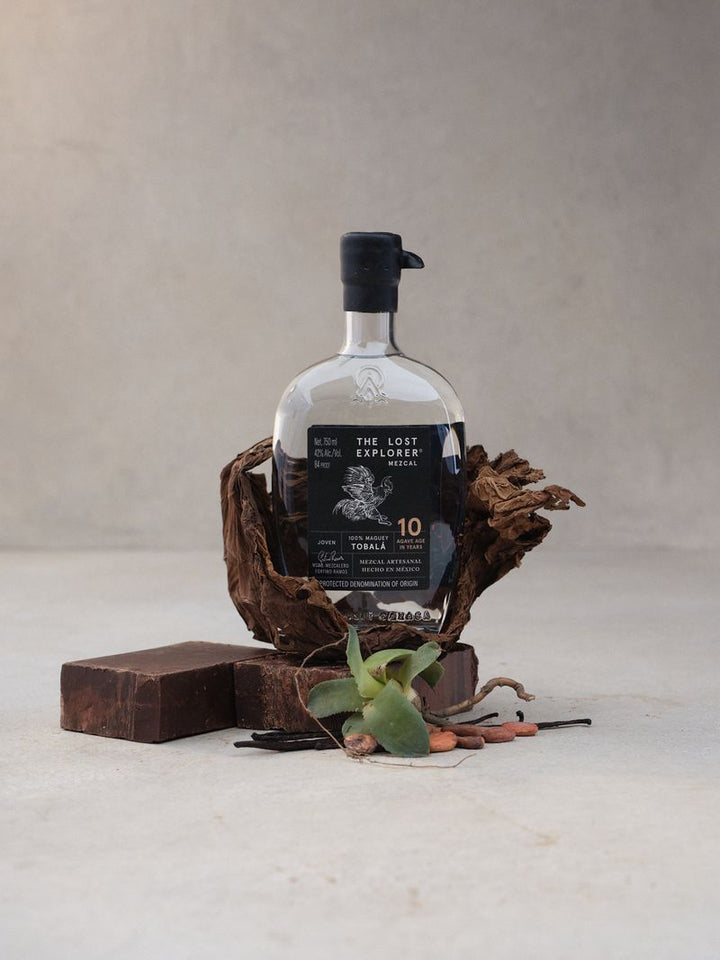 Bottle of 'The Lost Explorer' mezcal on a textured surface with decorative elements.