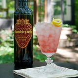 Bottle of Chambelyzette aperitif and a pink cocktail with lemon twist on a table outdoors.