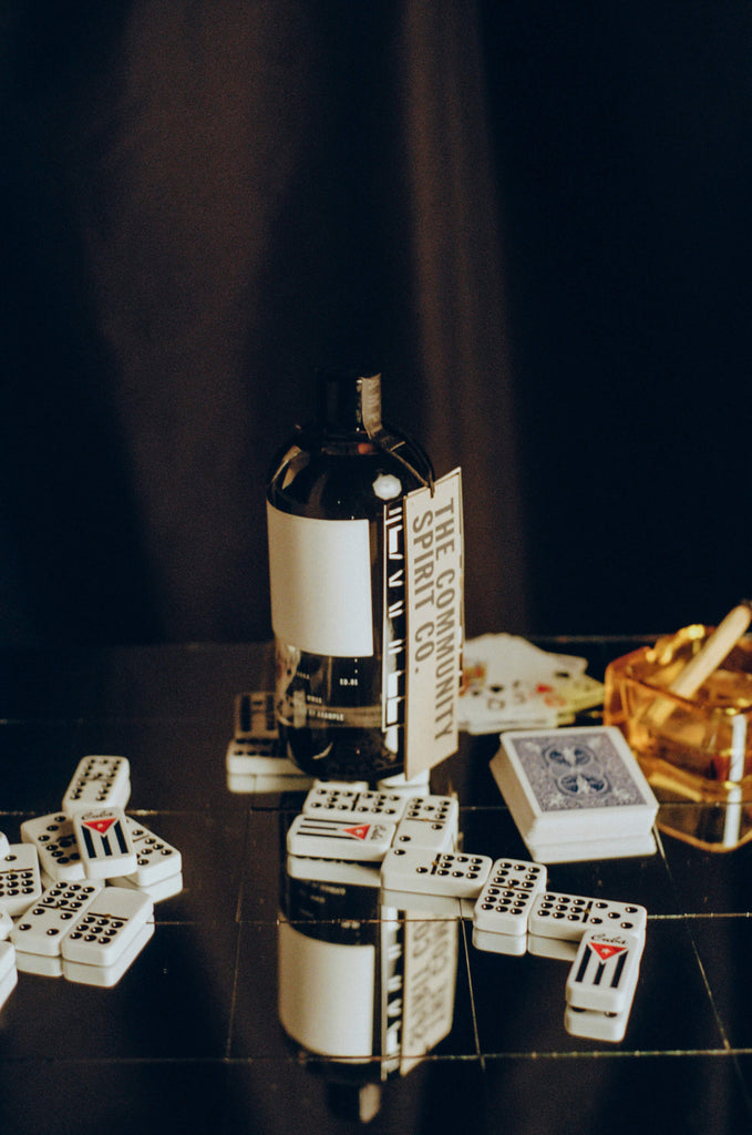 Bottle of The Community Spirit Vodka on a table next to a cocktail dominoes and playing cards.