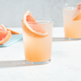A light pink Paloma cocktail in a short glass with a grapefruit slice on a table.
