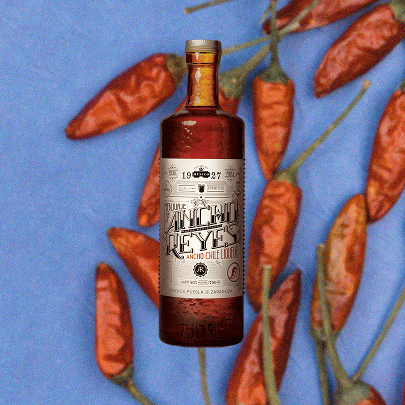 Bottle of Ancho Reyes Chili liqueur over a background of chilis