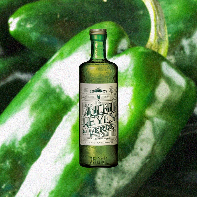 Bottle of Ancho Reyes Verde Chile Poblano Liqueur over blurred background of green chilis