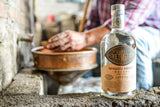 Corte Vetusto Espadin Mezcal on a stone wall with a man washing an item in a sink outdoors in the background.