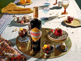 Bottle of Averna Amaro on a table with two cocktails and desserts on elegant plate ware.
