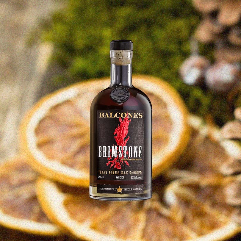 Bottle of Balcones Brimstone Whisky over a blurred background of dried orange slice garnishes.