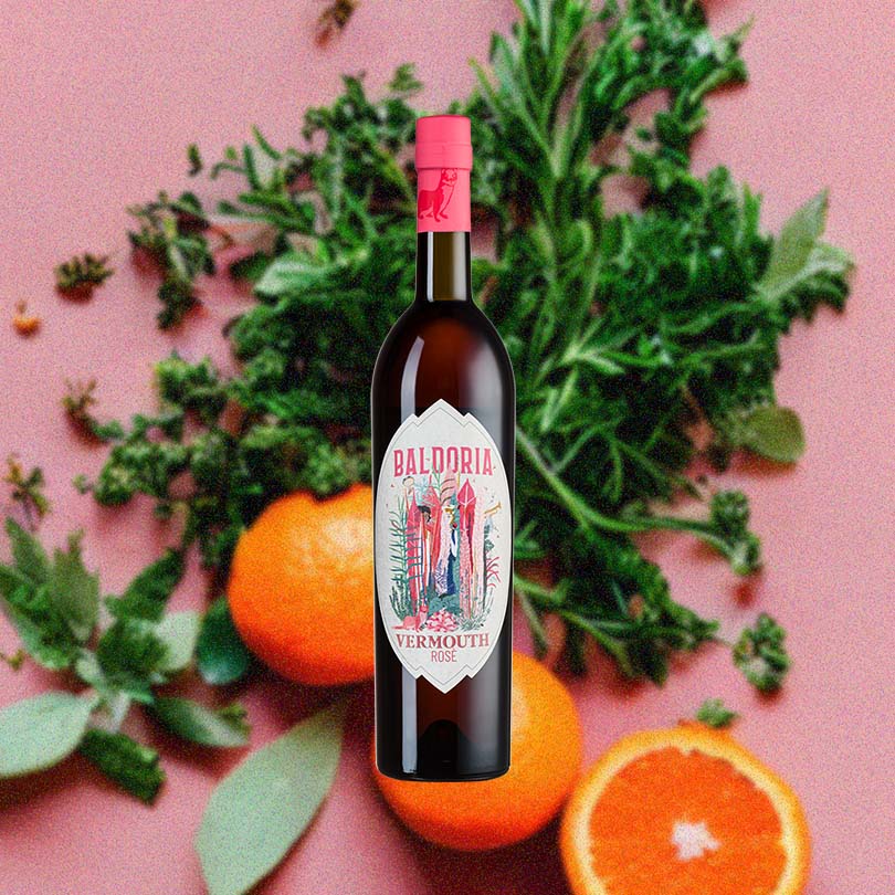 Bottle of Baldoria Rosé Vermouth over background image of oranges and green herbs.