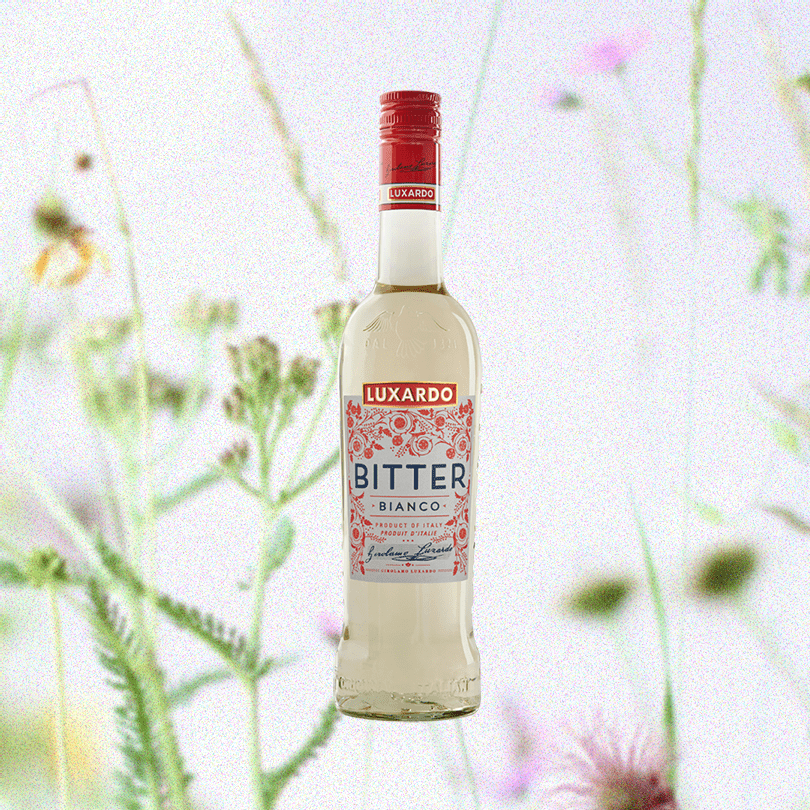 Bottle of Luxardo Bitter Bianco Liqueur over a very light backdrop of sparse flowers