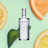 Bottle of The Botanist Islay Dry Gin over backdrop of a mint leaf, and orange and lemon slices.