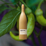 Bottle of Bozal Mezcal Espadin over back drop of green chilis.