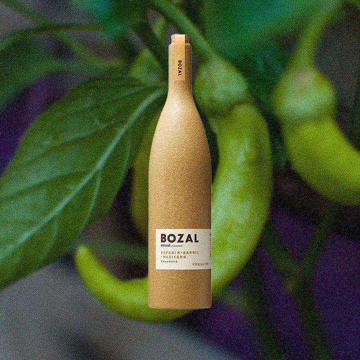 Bottle of Bozal Mezcal Espadin over back drop of green chilis.