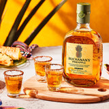 Bottle of Buchanan's Pineapple on a cutting board with 3 shots of alcohol on the table.