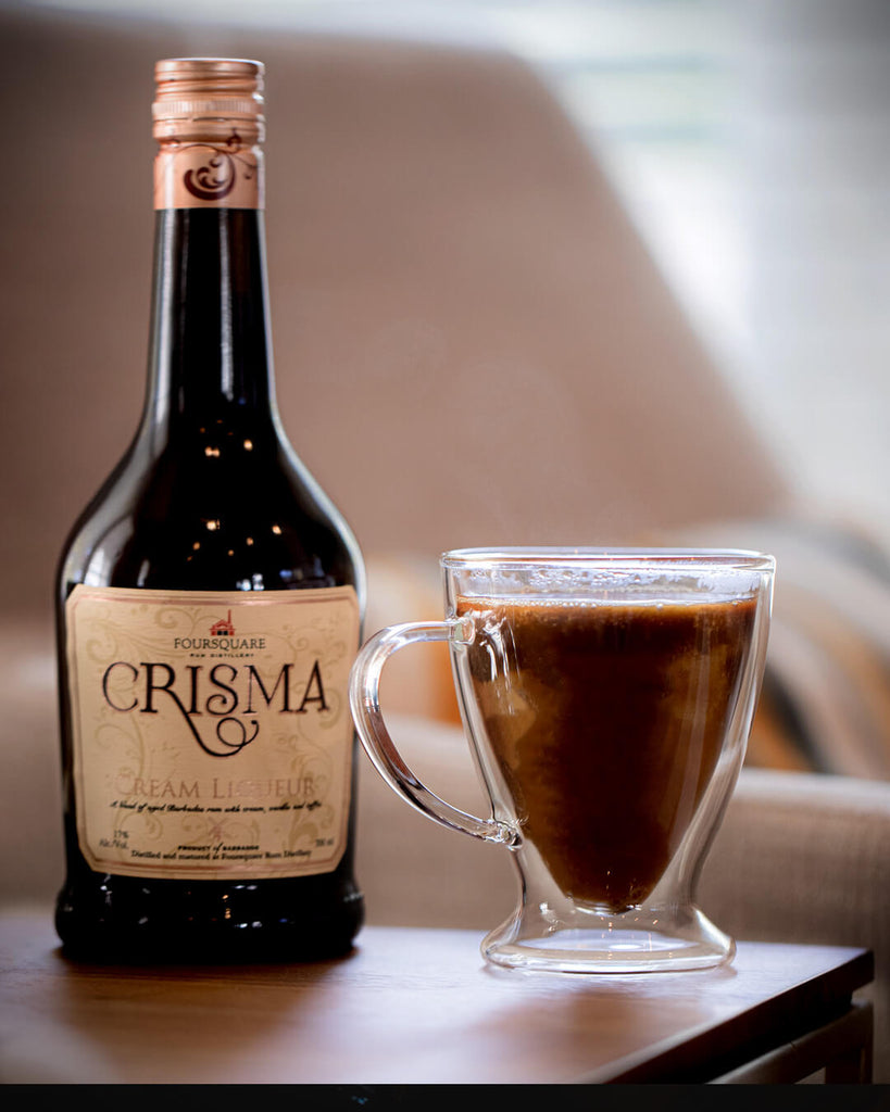 A bottle of Foursquare Crisma Rum Cream to the right with a glass mug full of a dark chocolatey-looking cocktail to the left