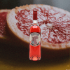 Cocchi Americano Rosa Aperitivo bottle over a backdrop of a sliced Grapefruit