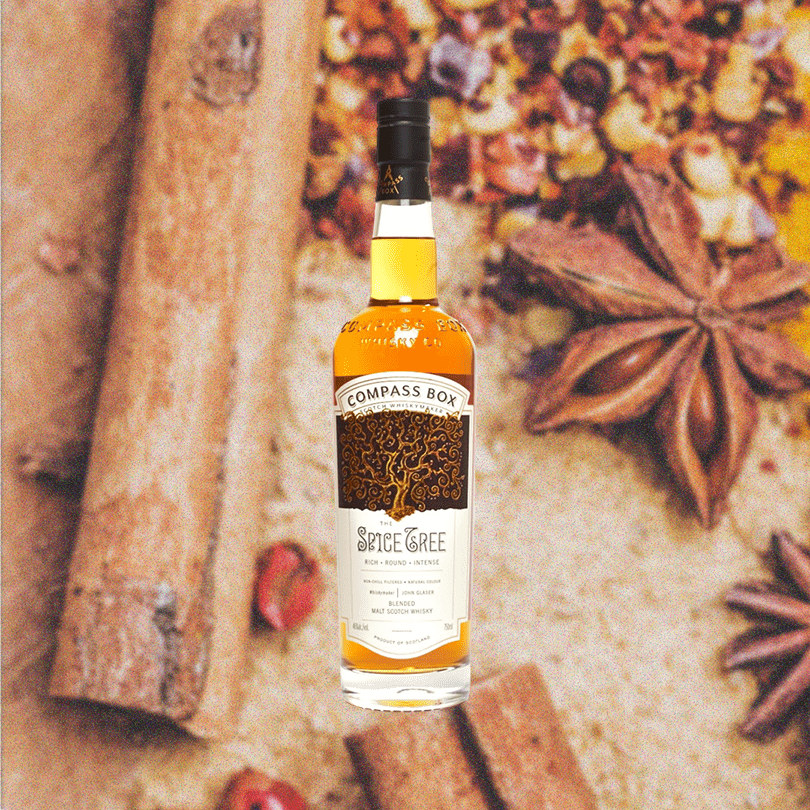 Bottle of Compass Box The Spice Tree Blended Malt Scotch Whisky. Backdrop of table with spices for baking.