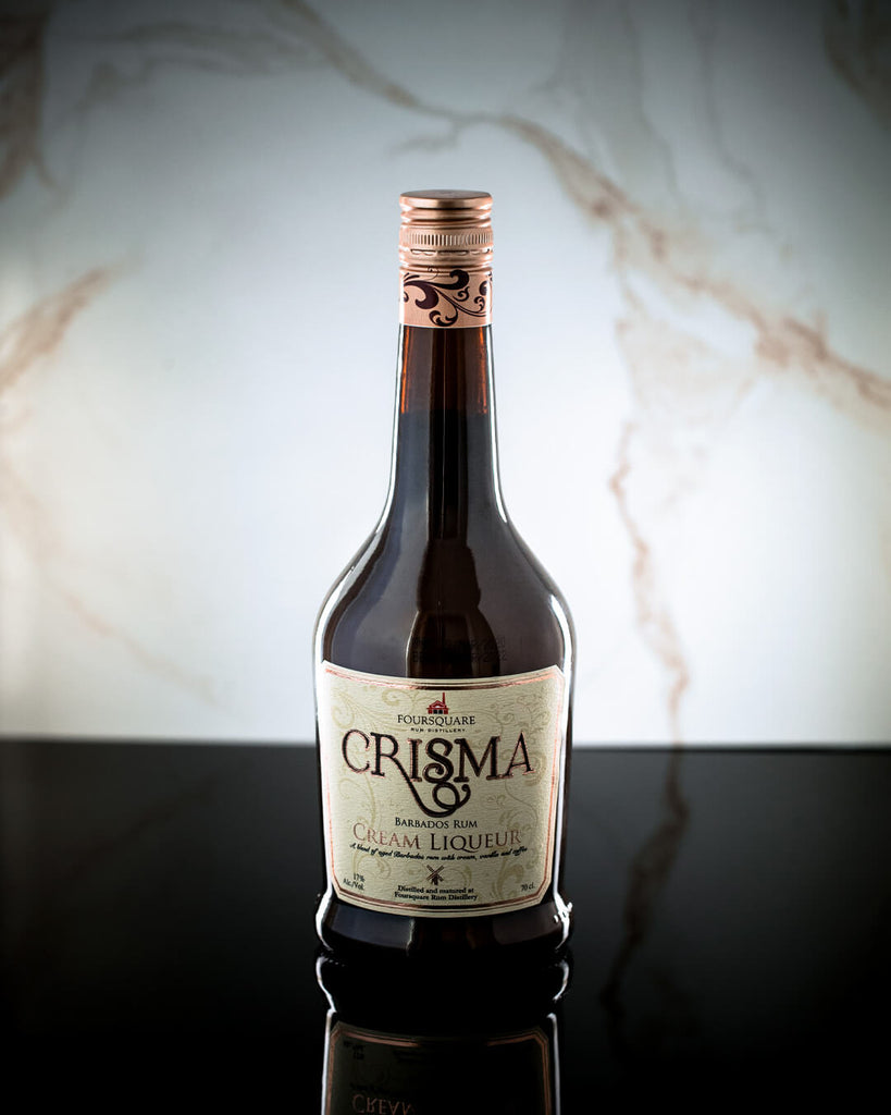 A bottle of Foursquare Crisma Rum Cream center on a black countertop with a marble background.