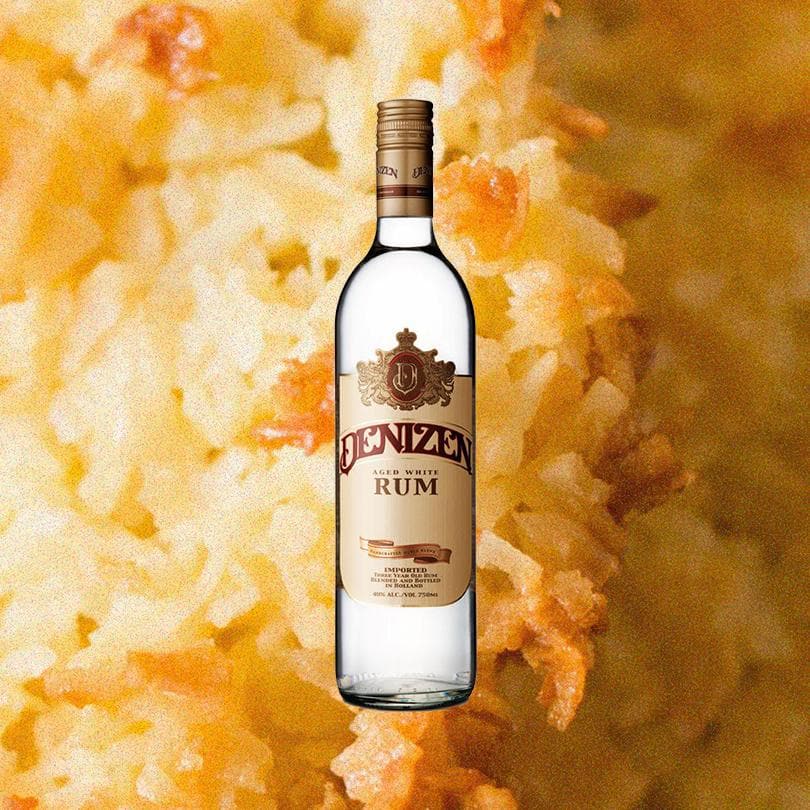 Bottle of Denizen Aged White Rum over backdrop of golden macaroons up close.