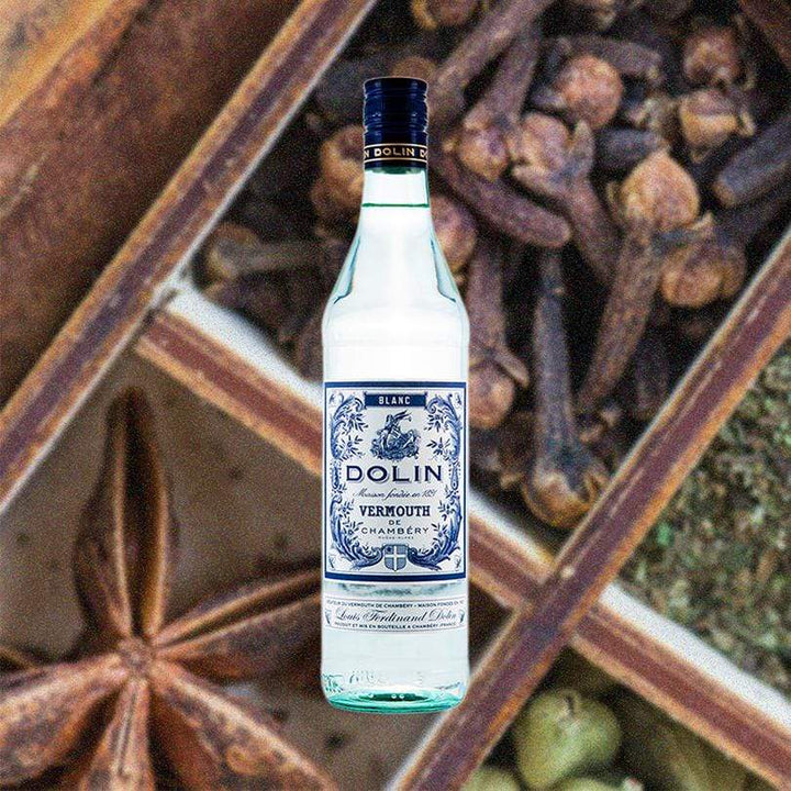 Bottle of Dolin Vermouth Blanc over backdrop of boxes of spices.