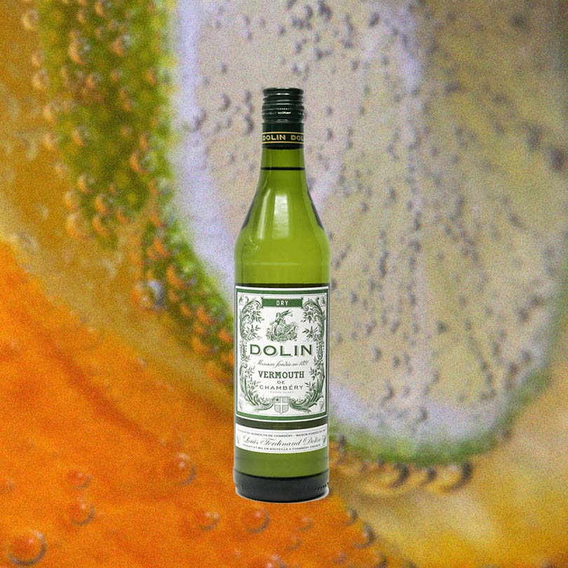 Bottle of Dolin Dry Vermouth De Chambéry over backdrop of lime wheel close up in soda water.