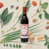 Bottle of Dolin Rouge Vermouth de Chambéry, over blurred wallpaper of flowers, leaves and spices.