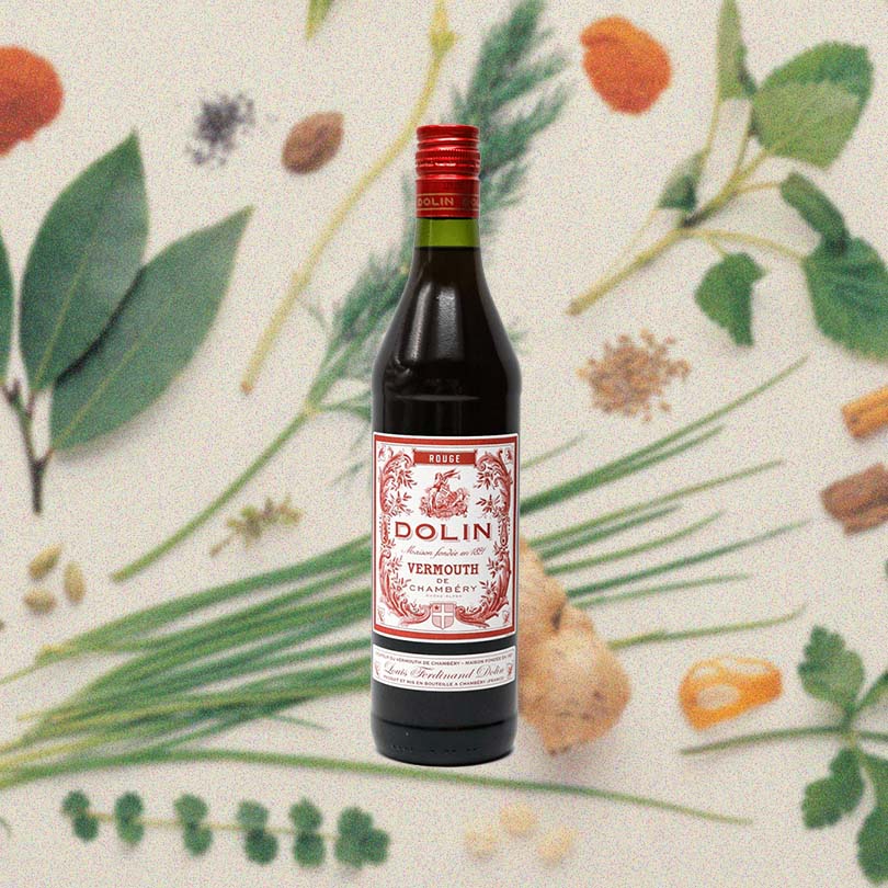 Bottle of Dolin Rouge Vermouth de Chambéry, over blurred wallpaper of flowers, leaves and spices.