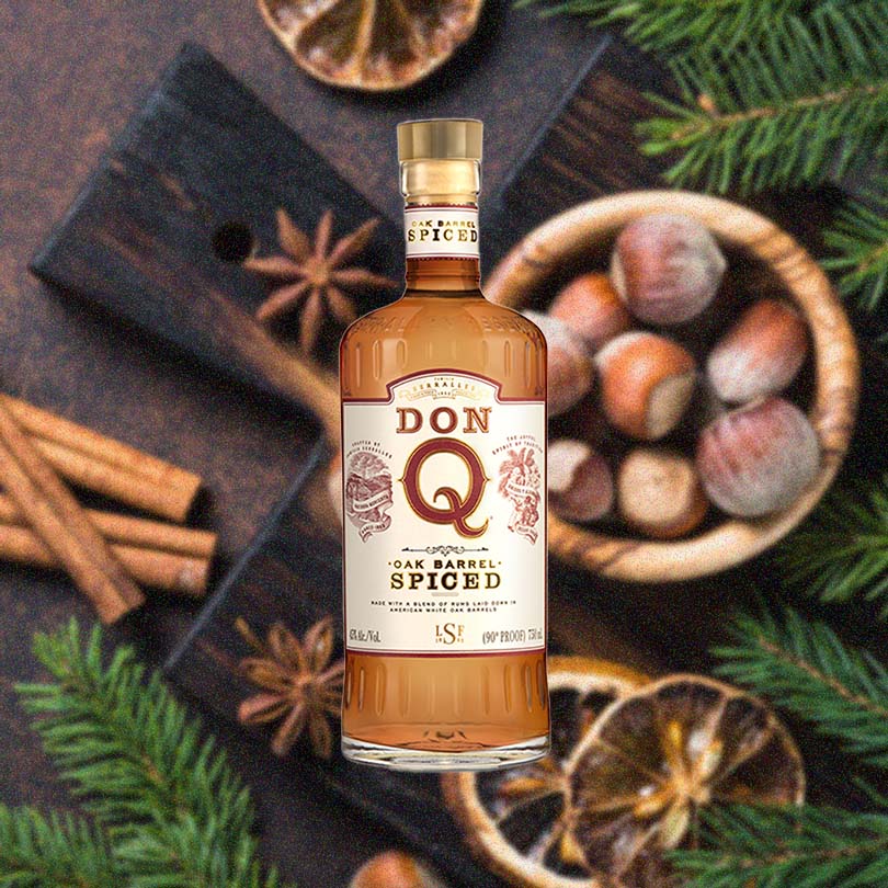Bottle of Don Q Oak Barrel Spiced Rum over back drop of table with nuts and spices.
