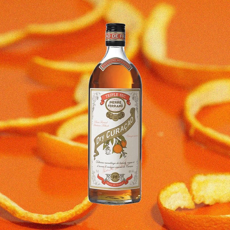 Bottle of Pierre Ferrand Dry Curacao over backdrop of orange rinds.
