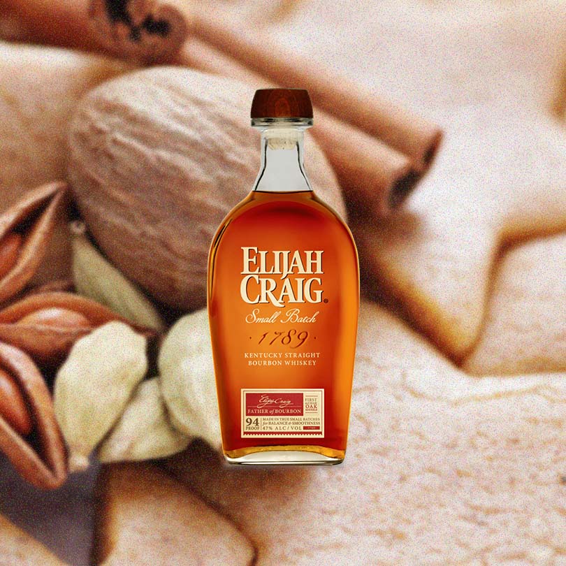 Bottle of Elijah Craig Small Batch Bourbon Whiskey over blurred background of nuts and spices.