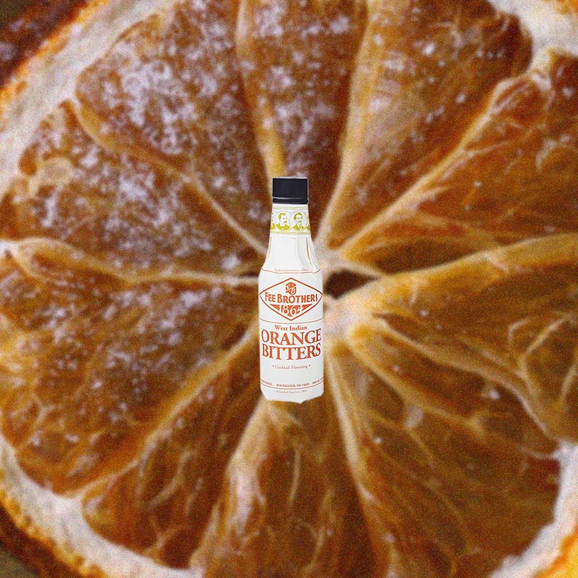 Bottle of Fee Brothers Orange Bitters over backdrop of a browning orange.