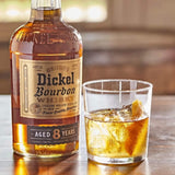 Bottle of George Dickel Bourbon Whisky Aged 8 Years on table next to glass with whiskey cocktail on the rocks with a lemon wedge.