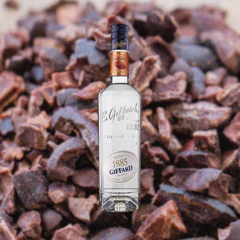 Bottle of Giffard Crème de Cacao Liqueur, over zoomed background of cacao nibs.
